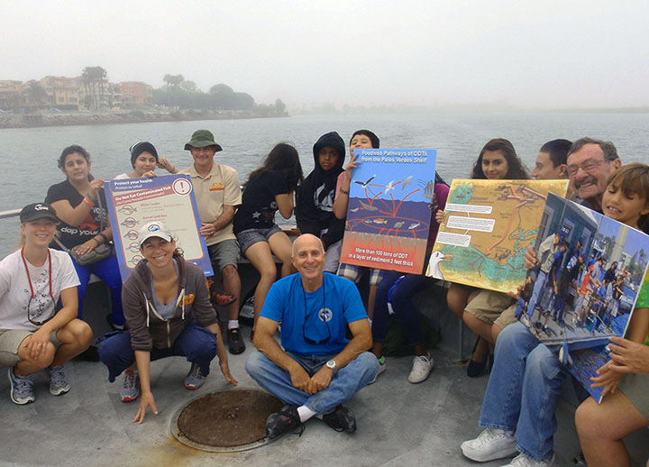Youth group on board a boat with volunteers from Marina Del Rey Anglers holding up foam board educational signs.