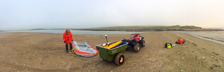 Man inflating boat next to ATV and woman kneeling on beach.