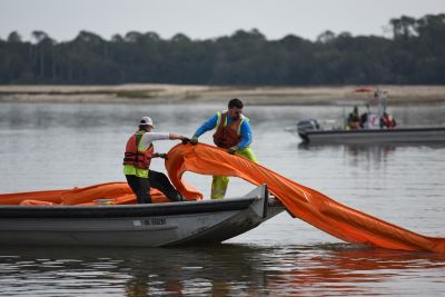 Two people distributing boom into the water from a small boat.