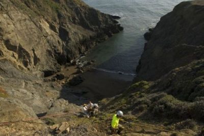 A wide shot of three people rappeling down to a pocket beach.