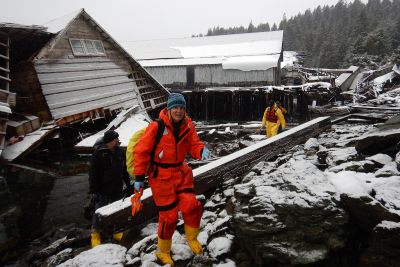 A woman in response gear with a collapsed structure behind her.