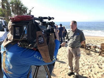 A camera crew filming a man on a beach.