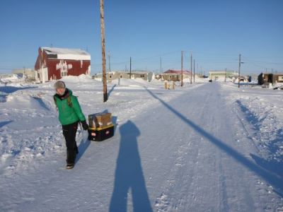 A woman dragging a gear box on a snowy street. 