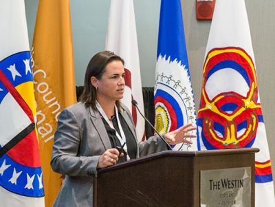 A woman standing at a podium with flags behind her.