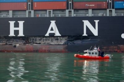 A small U.S. Coast Guard vessel in front of a gash in a container ship.