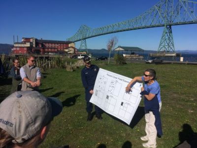 Two instructors hold up a diagram to explain to several students the percent cover of oil. Bridge in background.