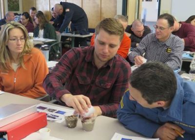 Three students work at a table with cups of sand and oil.