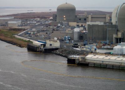 Yellow containment boom floats on a river next to a nuclear power plant.