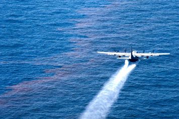 Aircraft flying over oil on water, applying a spray of dispersant.