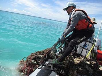 A man pulls a net out of the ocean into a small boat.