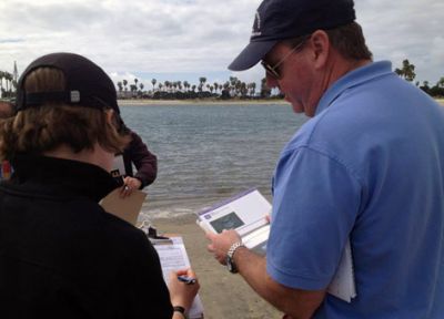 Two people looking at forms and a booklet on the beach.