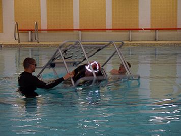 Coast Guard rolling a person in a simulated helicopter chair underwater.