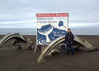 NOAA employee stands with bowhead whale bones and a welcome sign to Barrow.