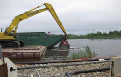 Mechanical shovel scooping mud from river's edge.