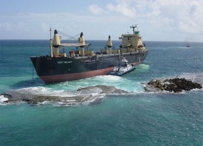 Large ship on reef with small boat beside it.