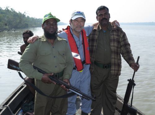 A man posing with two men holding guns on a boat.