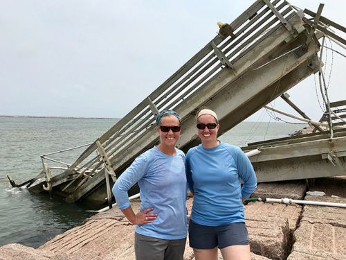 Two women standing in front of a collapsed structure. 