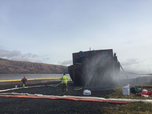 Abandoned barge, water spraying, oil boom on a beach.