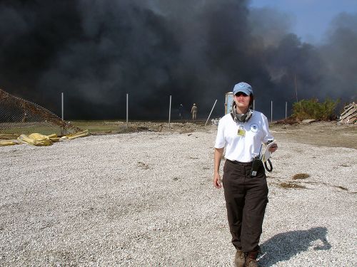 A woman walking toward the camera with smoke billowing behind her. 