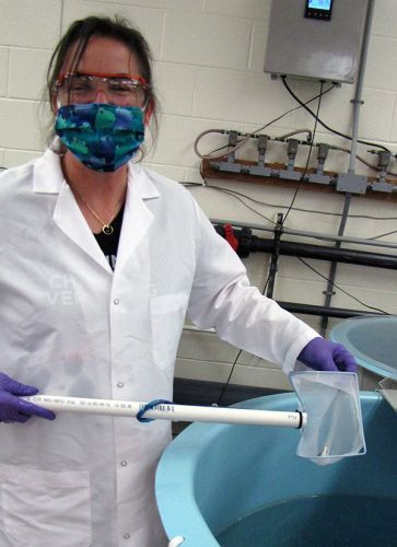 Woman in a mask and white coat next to a tank.