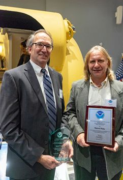 Two people posing with an plaque. 