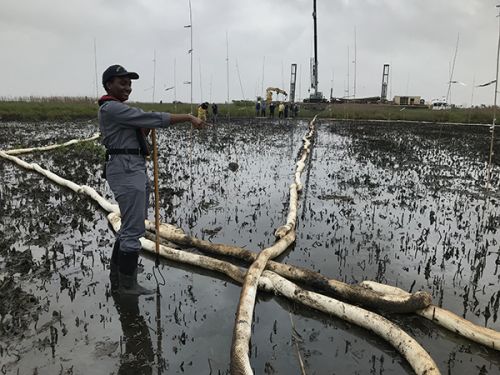 Woman standing in a marsh with thick hoses. 