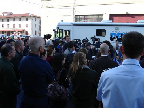 A group of people and press gather around a media vehicle.