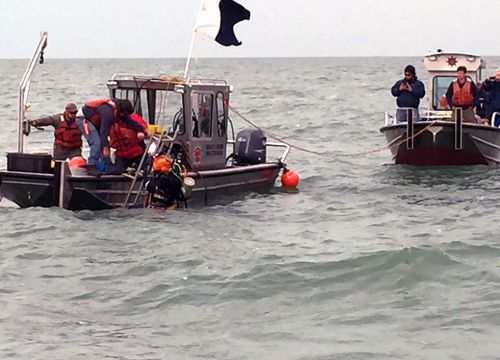U.S. Coast guard and others investigating oil leaking from the Argo, which sunk in 1937. Located on the U.S. side of the border with Canada, the wreck of the Argo was traced to reports of pollution on Lake Erie in both nations, indicating that the Argo was leaking. At the time of the sinking, the barge was reportedly loaded with 4,762 barrels of crude oil and the chemical benzol. Two boats on the water.