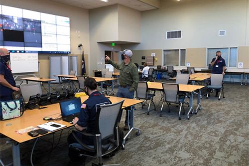 People at tables in a classroom facing a large screen.