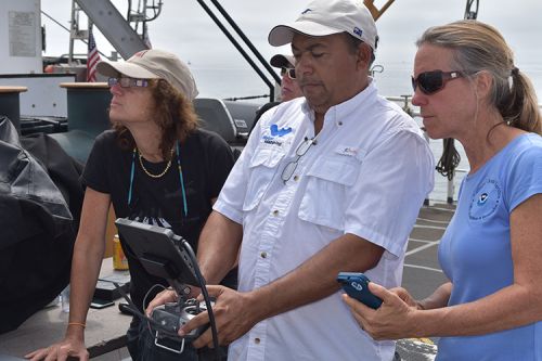 A group of people on a boat looking at a screen. 