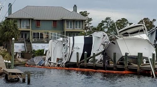 Damaged and displaced boats and other debris in the water, in front of a large home.