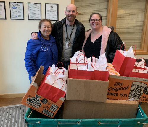 Three people posing with boxes of gift bags. 