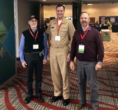 Three men pose for photo.