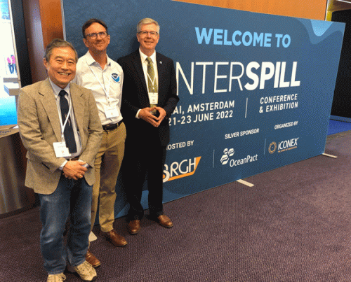 Three people pose for a photo next to a sign reading "Interspill."