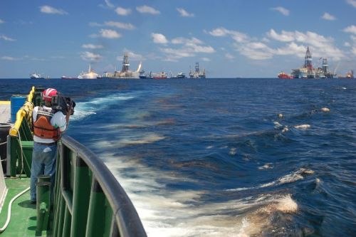 A cameraperson on a vessel in oiled waters.