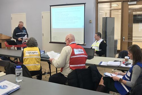 People in brightly colored vests sitting in a conference room watching a speaker. 