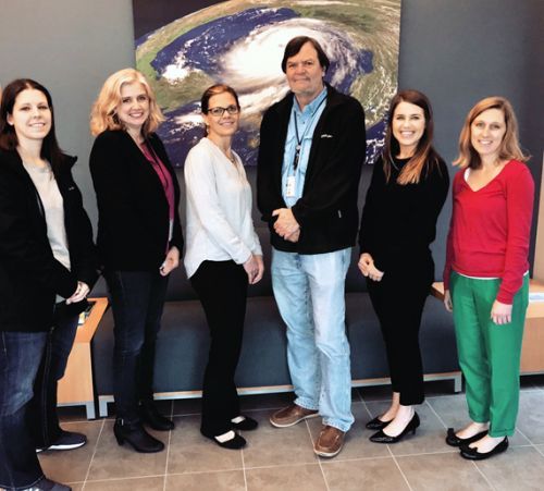 Six people standing in front of a print of a satellite image of a hurricane.