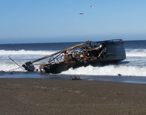 Vessel on its side in the waves at the edge of the beach.