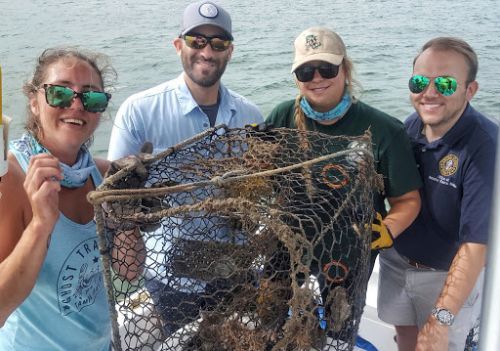 Four people posing with crab pot and debris.