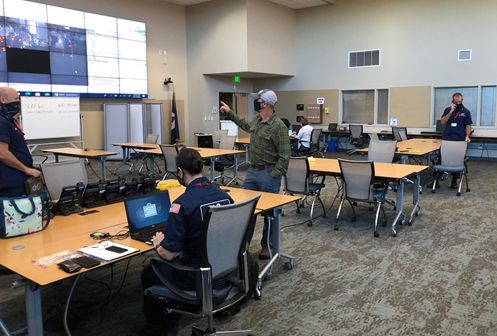 People at tables in a classroom facing a large screen.