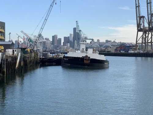 Barge listing with city buildings in background.