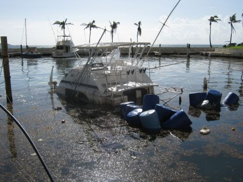 Small vessel, partially submerged in the water with blue barrels floating around it. 