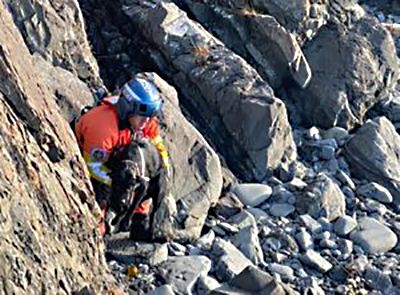 Man climbing down a rocky sloe, holding a dog.