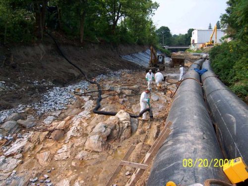 Workers in a streambed, next to two large pipes.