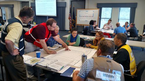 A group of people in different colored vests sitting at a table. 