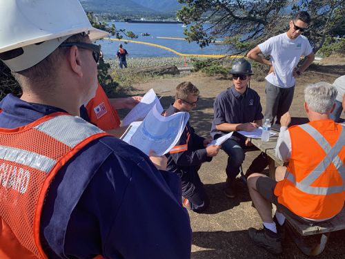 A group of people in response gear on a shoreline talking. 