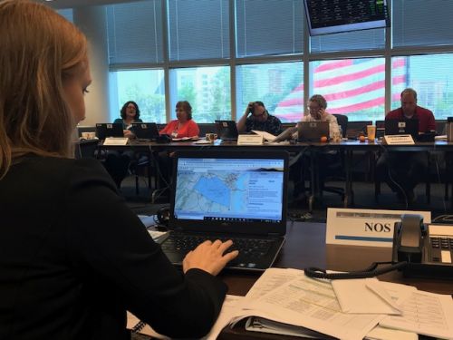 A woman looking at a map on a computer sitting across from a group of people at another table. 