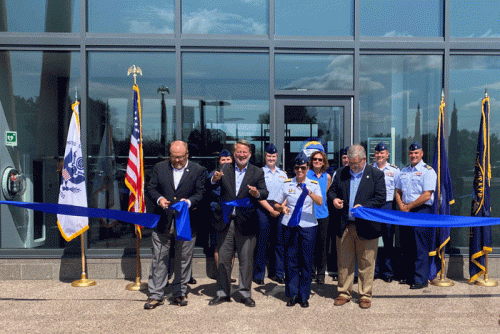 A group of people cutting a blue ribbon in front of a building.