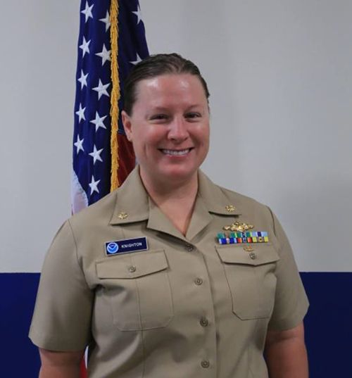 Woman in uniform posing for photo with a flag.