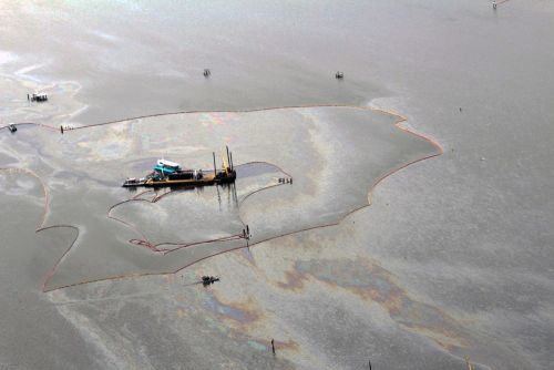 Vessel in water surrounded by smaller boats and oil slicks.